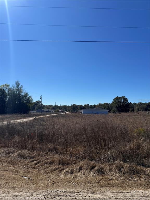 A vacant, grassy lot features a dirt road and a distant house under a clear sky — TBD SW 150TH COURT, OCALA, FL