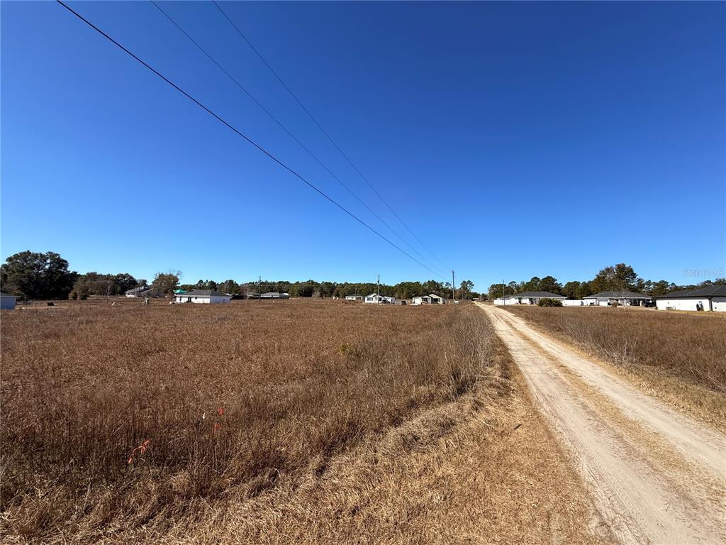 A dirt road runs alongside a large, dry, grassy field with houses in the distance — TBD SW 150TH COURT, OCALA, FL