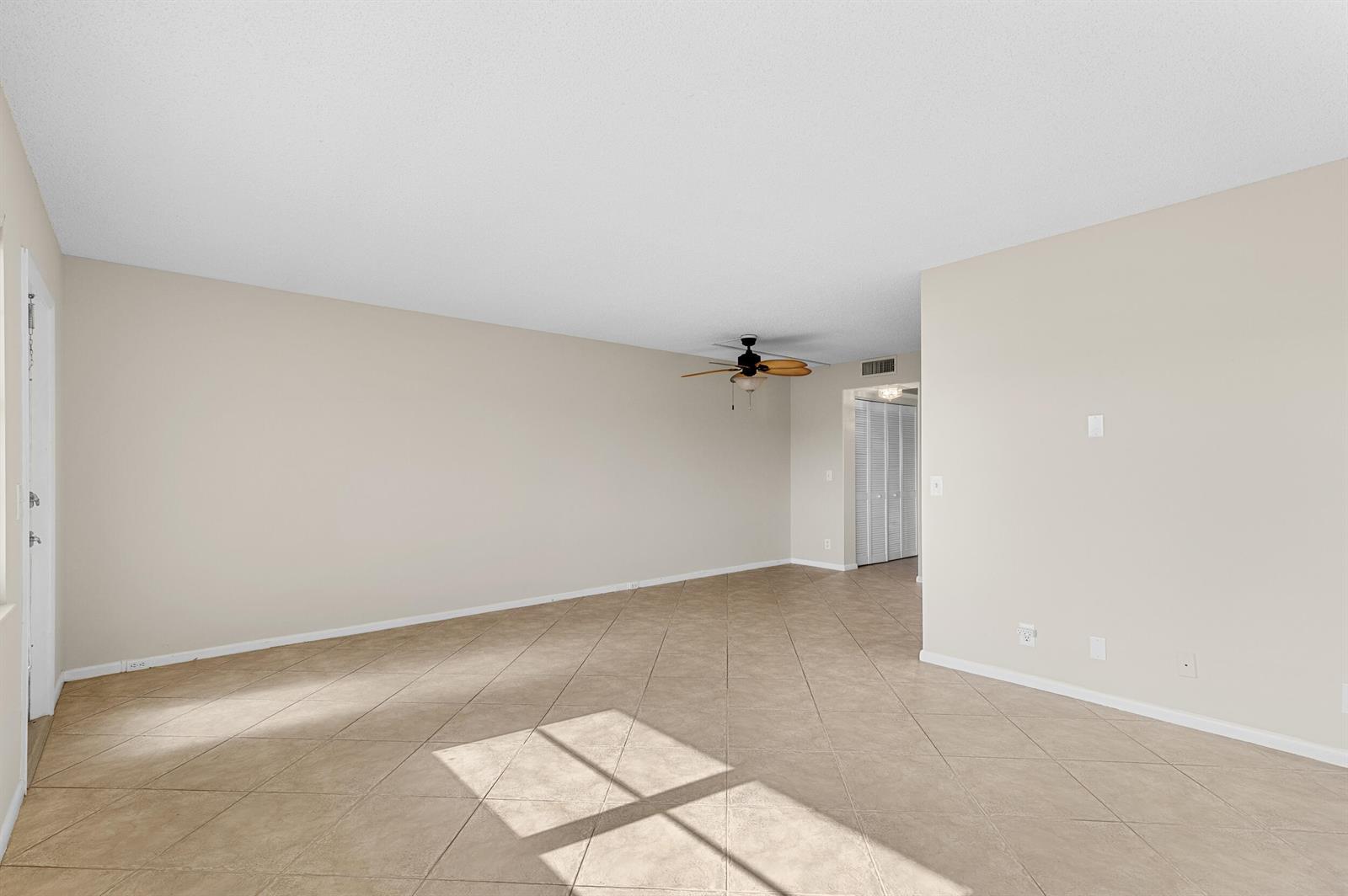 An empty living room features beige walls, a ceiling fan, and diagonal tile flooring — 3013 Wolverton A, Boca Raton FL 33434, BOCA RATON, FL