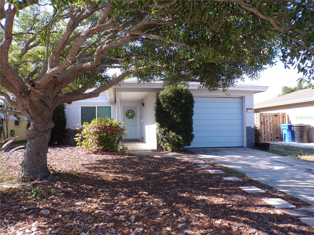 A single-story house features a light blue garage door, a front entrance, and a large tree — 6550 3RD AVENUE S, ST PETERSBURG, FL