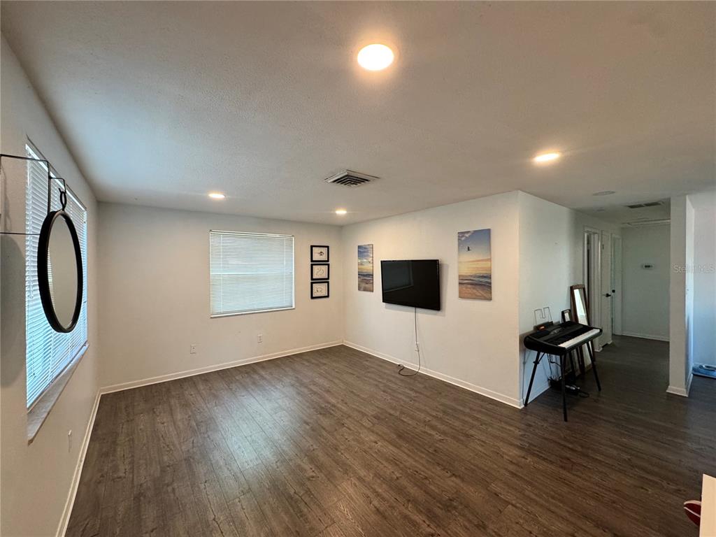 A living room features wood-look flooring, a wall-mounted television, and a keyboard on a stand — 6550 3RD AVENUE S, ST PETERSBURG, FL