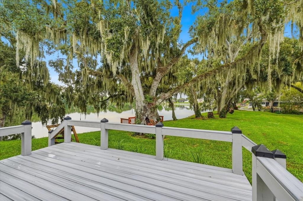 A wooden deck overlooks a grassy lawn, large mossy trees, and a calm lake — 6760 LAKE CLARK DRIVE, LAKELAND, FL