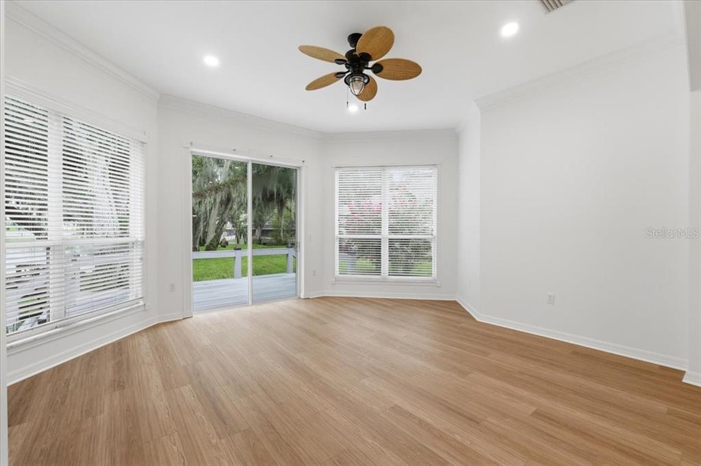 A bright, empty room features light wood-look flooring, white walls, a ceiling fan, and sliding doors — 6760 LAKE CLARK DRIVE, LAKELAND, FL