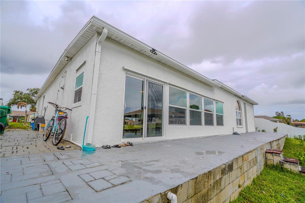 A white stucco house exterior features a gray concrete patio and a sliding glass door — 2145 PORPOISE STREET, MERRITT ISLAND, FL