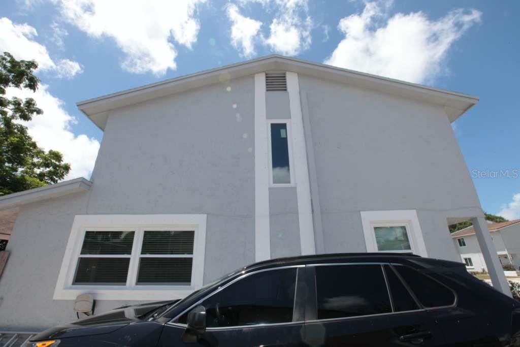 A low-angle exterior view of a light gray two-story house with a black car parked — 2073 SAN SEBASTIAN WAY N, CLEARWATER, FL