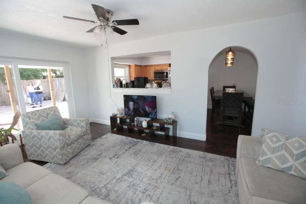 A living room features a ceiling fan, a television console, and an arched dining entrance — 2073 SAN SEBASTIAN WAY N, CLEARWATER, FL