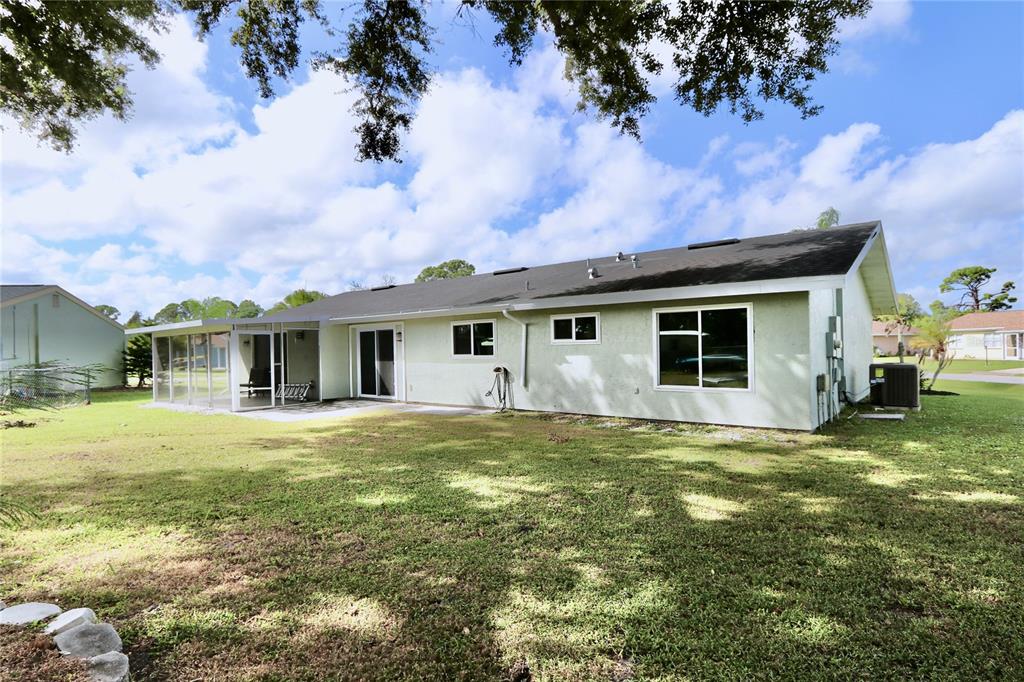 The back exterior of a light green house features a screened-in patio and large windows — 6796 ELECTRA AVENUE, NORTH PORT, FL