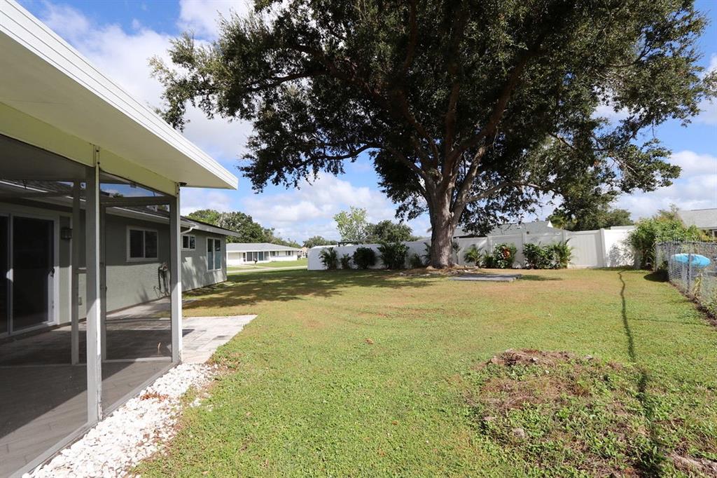 A grassy backyard features a large oak tree, a white fence, and a screened patio — 6796 ELECTRA AVENUE, NORTH PORT, FL