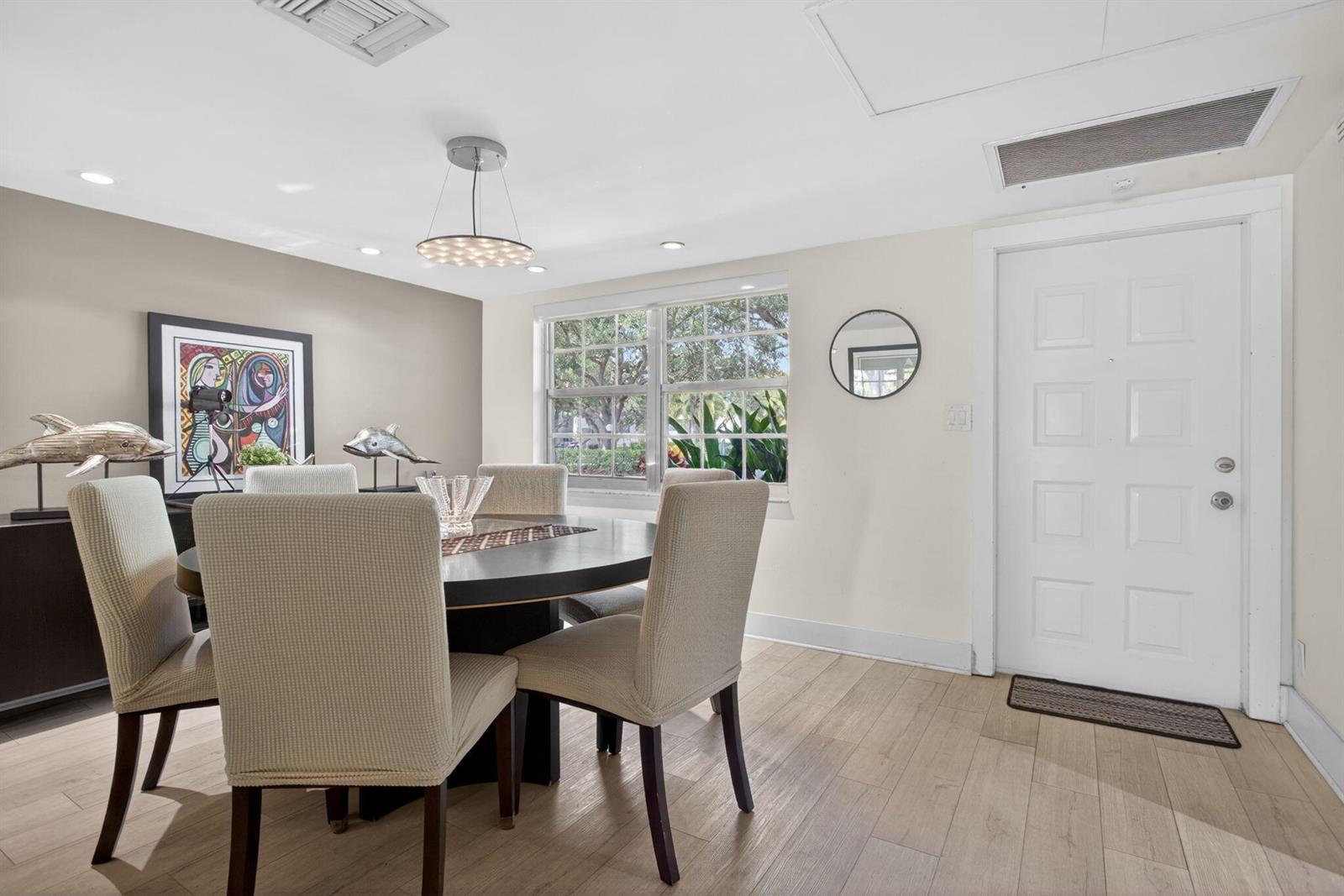 A dining room features a round table, upholstered chairs, light wood flooring, and a door — 901 W Cypress Lane # 103, Pompano Beach FL 33069, POMPANO BEACH, FL