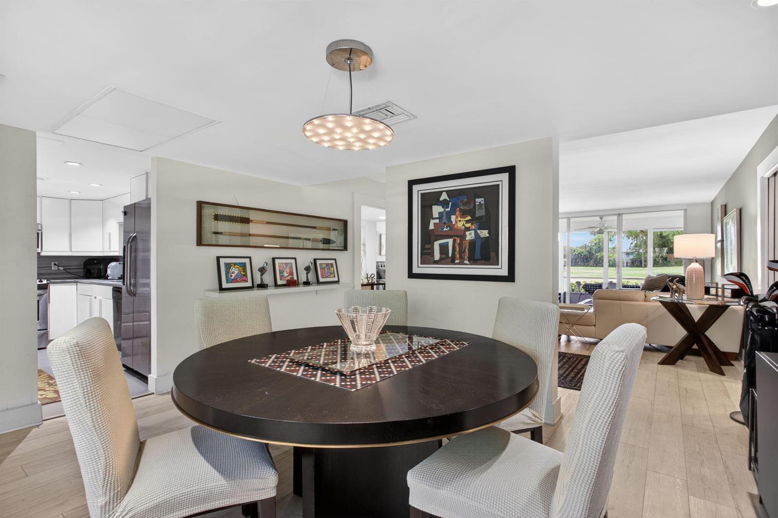 A dining room features a round dark wood table, upholstered chairs, and modern pendant lighting — 901 W Cypress Lane # 103, Pompano Beach FL 33069, POMPANO BEACH, FL