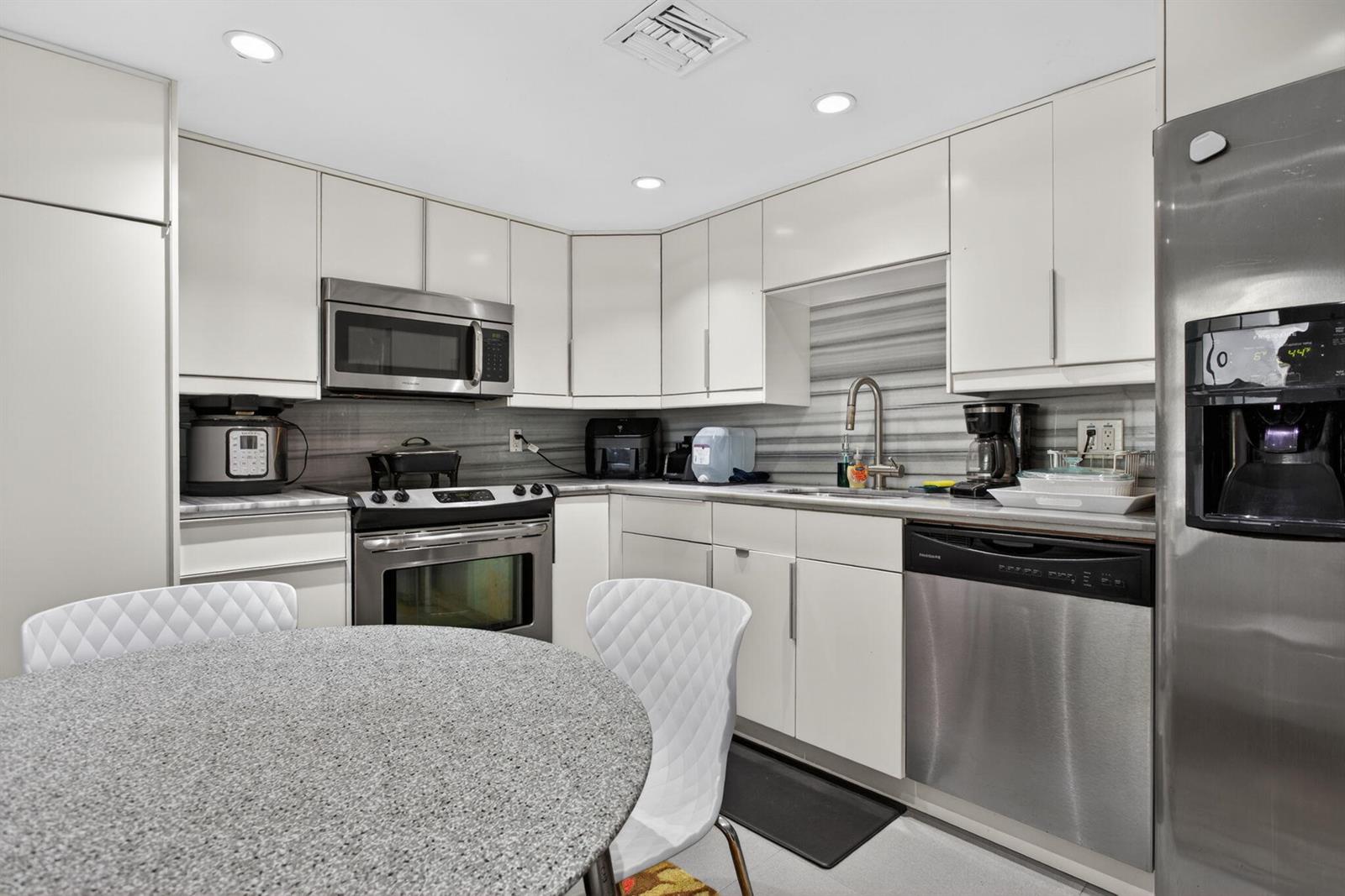 A kitchen features white cabinetry, stainless steel appliances, a gray backsplash, and a round table — 901 W Cypress Lane # 103, Pompano Beach FL 33069, POMPANO BEACH, FL