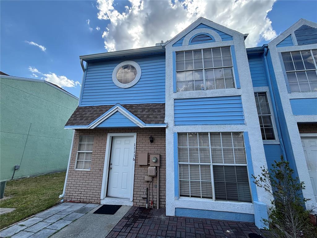 A two-story townhouse exterior features blue siding, brick accents, a front door, and multiple windows — 11116 ALDERLY, ORLANDO, FL