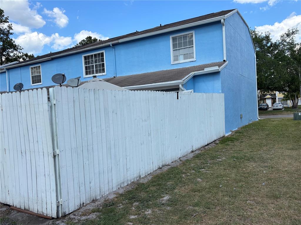 A bright blue two-story townhouse exterior features a white wooden privacy fence in the yard — 11116 ALDERLY, ORLANDO, FL