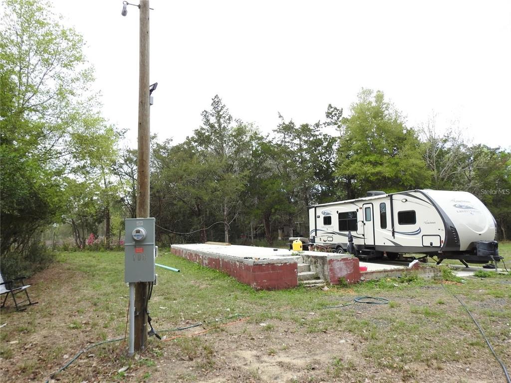 A travel trailer is parked next to a concrete slab on a wooded lot — 103 GEORGE DRIVE, INTERLACHEN, FL