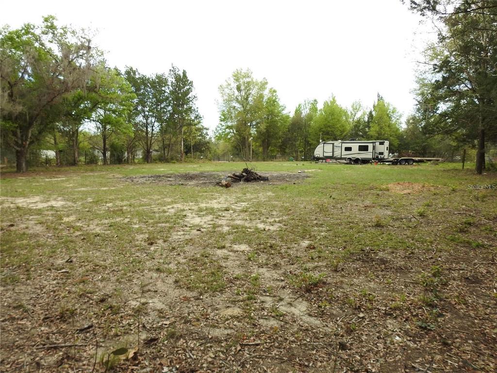 A large, grassy, wooded lot features a fire pit and a parked travel trailer — 103 GEORGE DRIVE, INTERLACHEN, FL