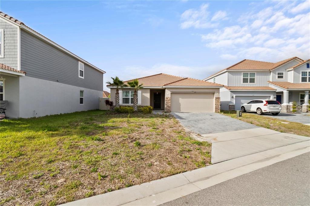 A single-story suburban house with a tan stucco exterior, tile roof, and paved driveway — 1154 OAK BLUFF DRIVE, DAVENPORT, FL