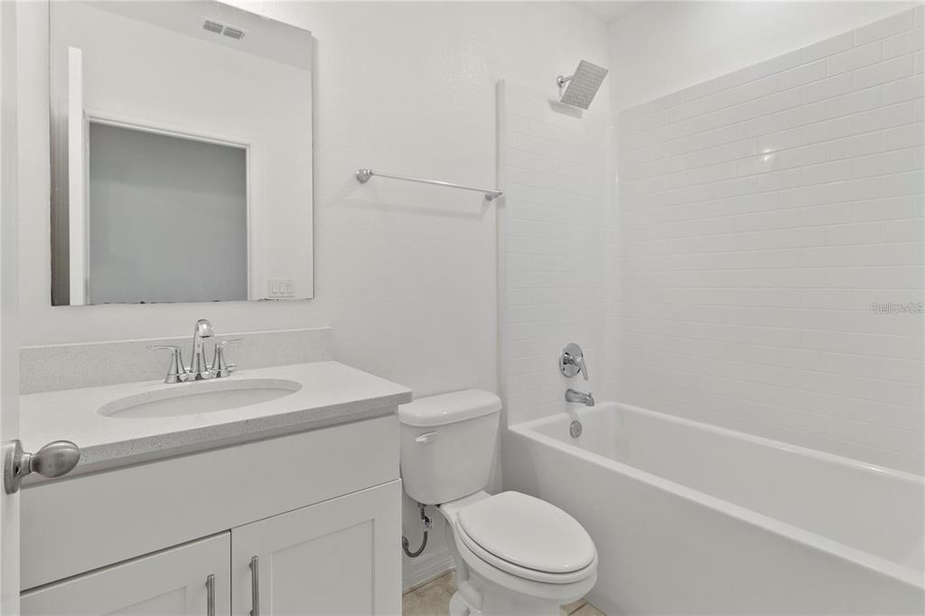 A bathroom features a white vanity, a toilet, and a tub with white subway tile — 1154 OAK BLUFF DRIVE, DAVENPORT, FL
