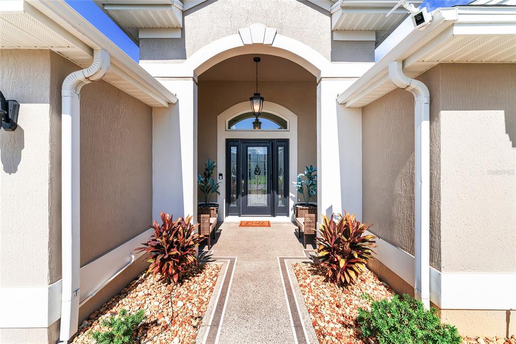 A covered entryway features a glass-paneled front door, potted plants, and a paved walkway — 3806 VIEW PATH, THE VILLAGES, FL