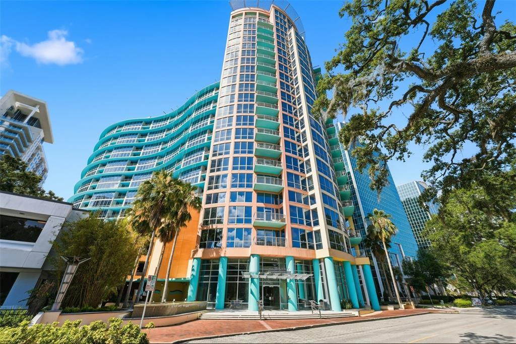 A tall, curved modern apartment building with teal accents and balconies stands under a sky — 322 E CENTRAL BOULEVARD UNIT 912, ORLANDO, FL