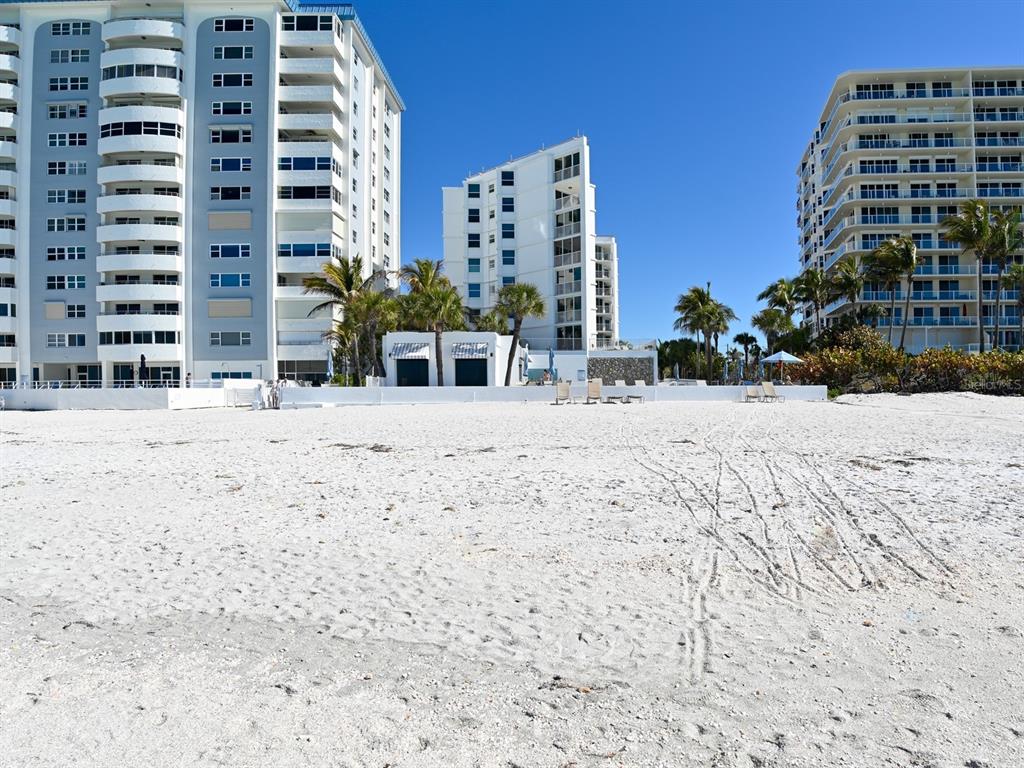 A sandy beach sits in front of several multi-story residential buildings under a clear sky — 1770 BENJAMIN FRANKLIN DRIVE UNIT 206, SARASOTA, FL