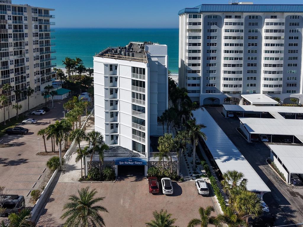 An aerial view shows a white multi-story apartment building situated near a beach and ocean — 1770 BENJAMIN FRANKLIN DRIVE UNIT 206, SARASOTA, FL