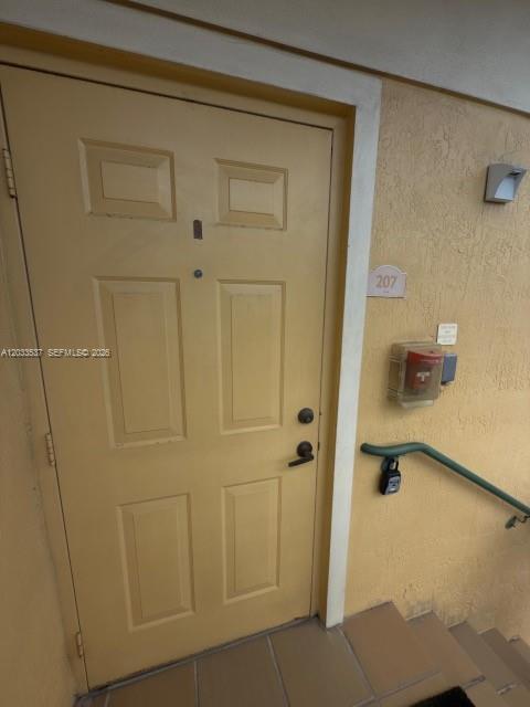 A yellow exterior door with a peephole and lockbox is positioned next to unit number 207 — DORAL, FL