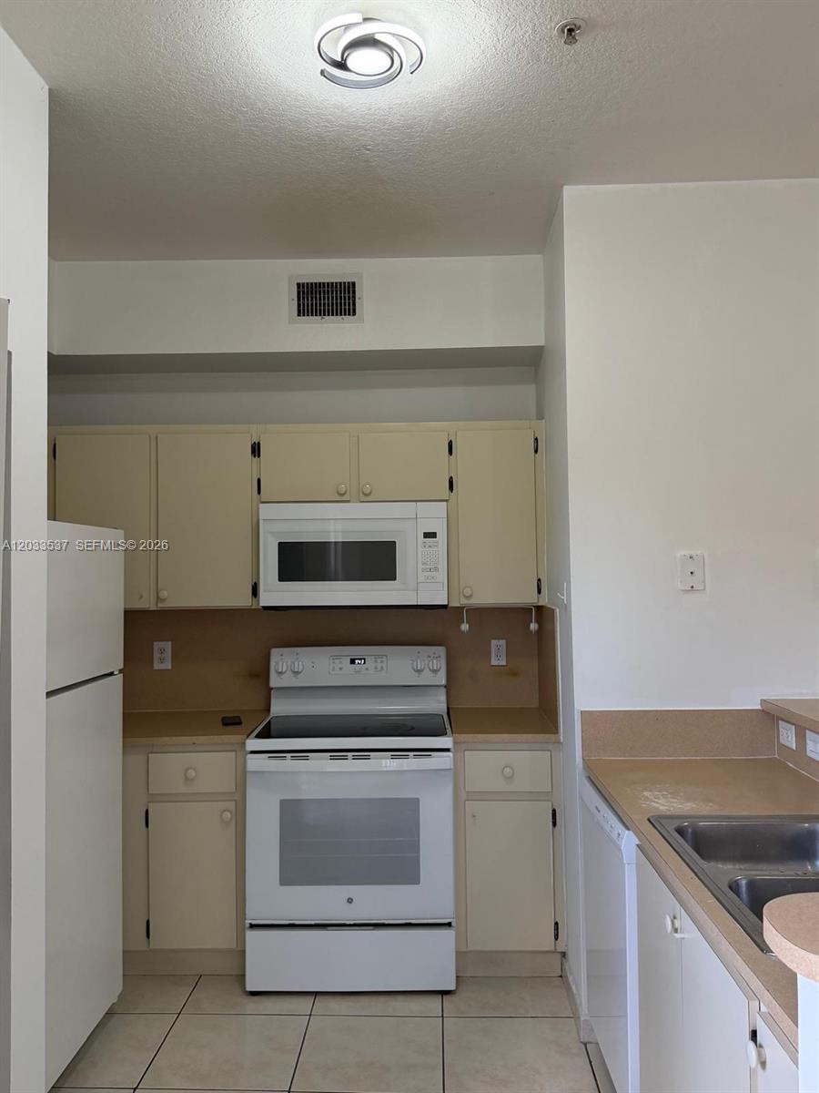 A kitchen features white appliances, light-colored cabinets, a tan backsplash, and tile flooring — DORAL, FL