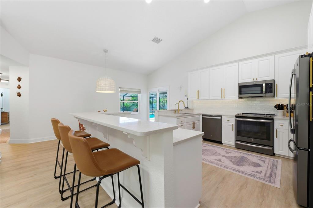 A modern kitchen features white cabinets, stainless steel appliances, and a breakfast bar with stools — 3347 LAKE SHORE LANE, CLEARWATER, FL