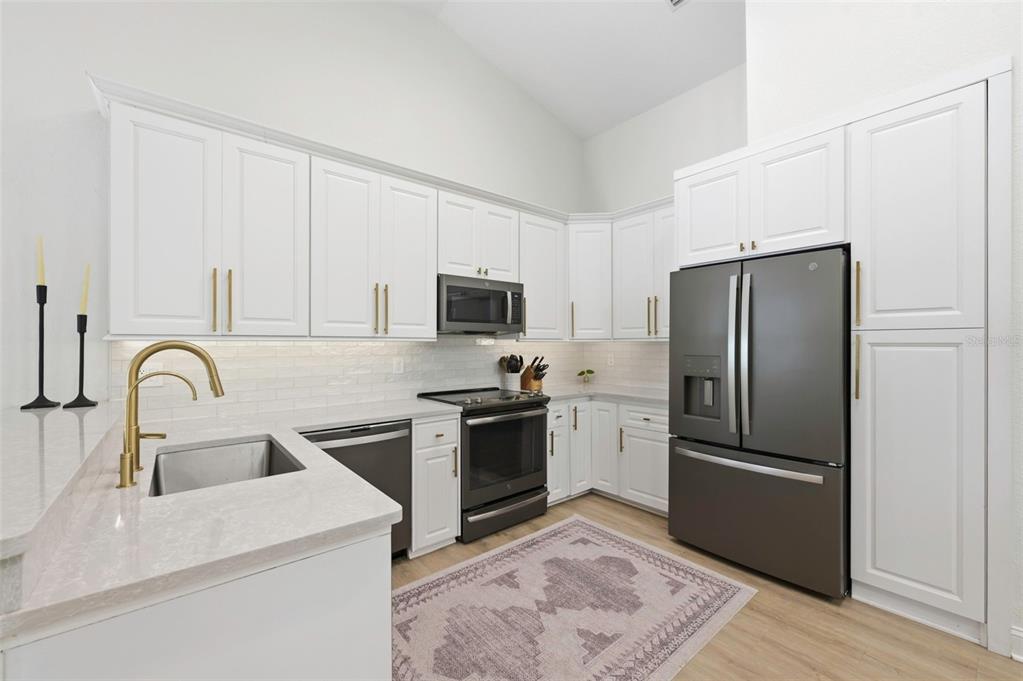 A kitchen features white cabinets, stainless steel appliances, gold hardware, and a light-colored countertop — 3347 LAKE SHORE LANE, CLEARWATER, FL