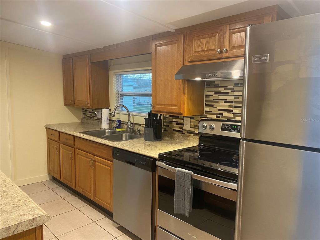 A kitchen features wood cabinets, stainless steel appliances, a tiled backsplash, and granite countertops — 26022 GLASGOW AVENUE, PUNTA GORDA, FL