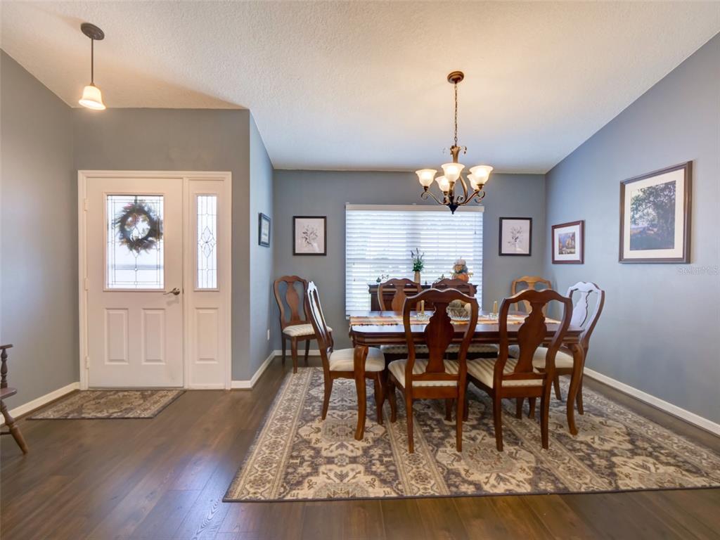 A dining room with a wooden table, six chairs, a chandelier, and a front door — 4704 RIVER RIDGE DRIVE, LEESBURG, FL