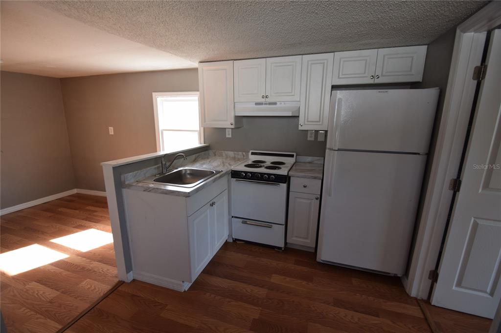 A kitchen features white cabinets, a white stove, a refrigerator, and a stainless steel sink — 1060 E WABASH STREET UNIT 1060 1/2, BARTOW, FL