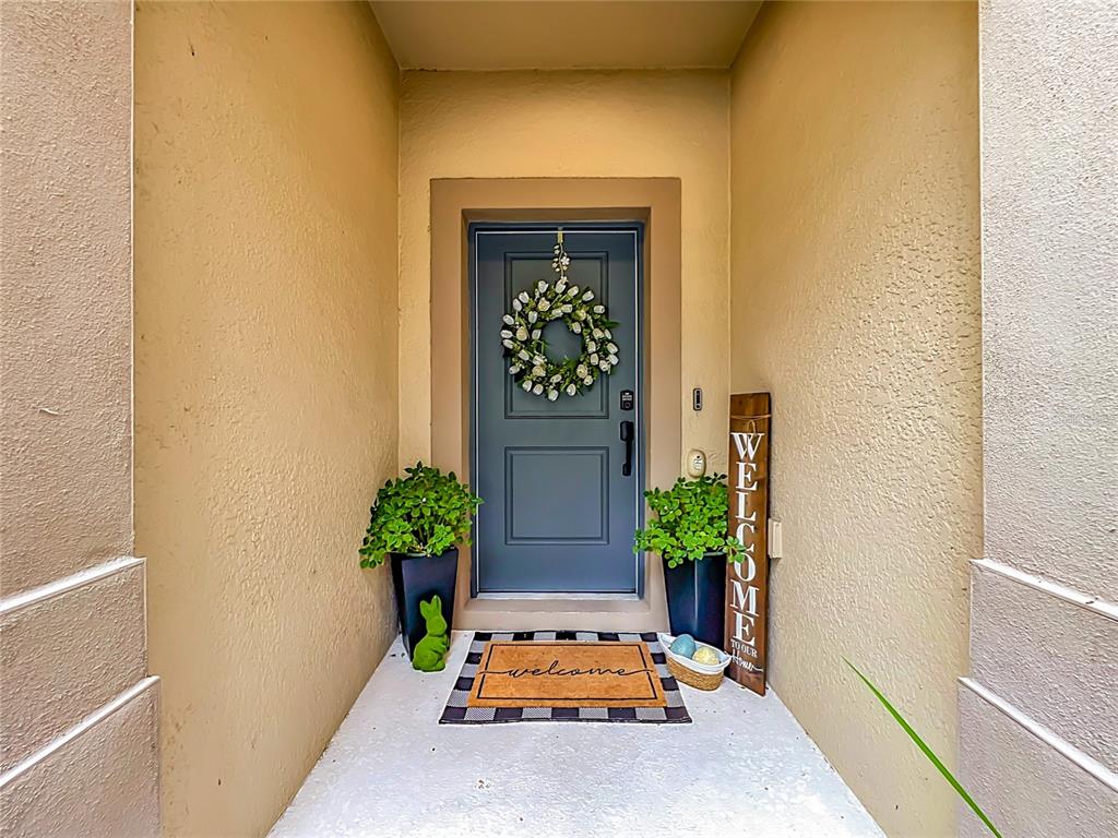 A blue front door with a wreath is framed by two potted plants and decor — 1084 PAVIA DRIVE, APOPKA, FL