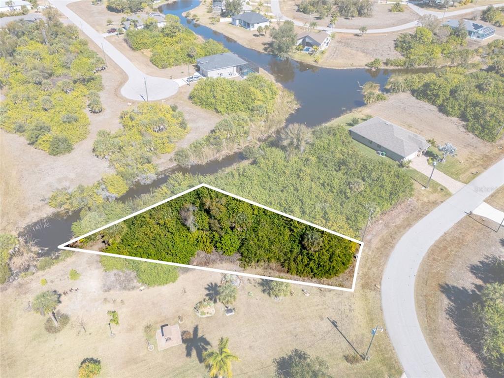 An aerial view shows a vacant, wooded lot outlined in white near a canal — 132 CREVALLE ROAD, ROTONDA WEST, FL