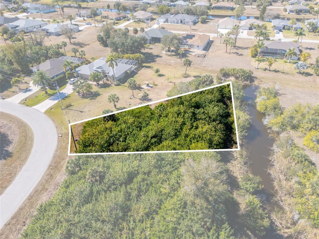 An aerial view shows a vacant, tree-covered residential lot outlined in white near a canal — 132 CREVALLE ROAD, ROTONDA WEST, FL