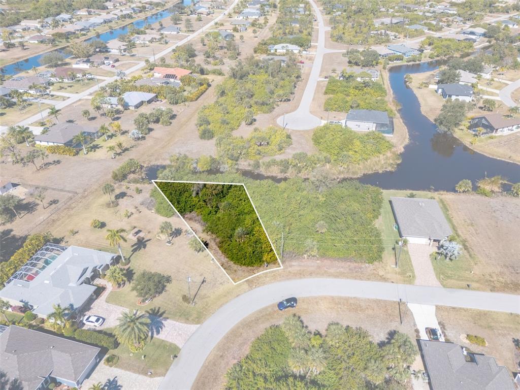 An aerial view shows a vacant, wooded residential lot outlined in white near a canal — 132 CREVALLE ROAD, ROTONDA WEST, FL