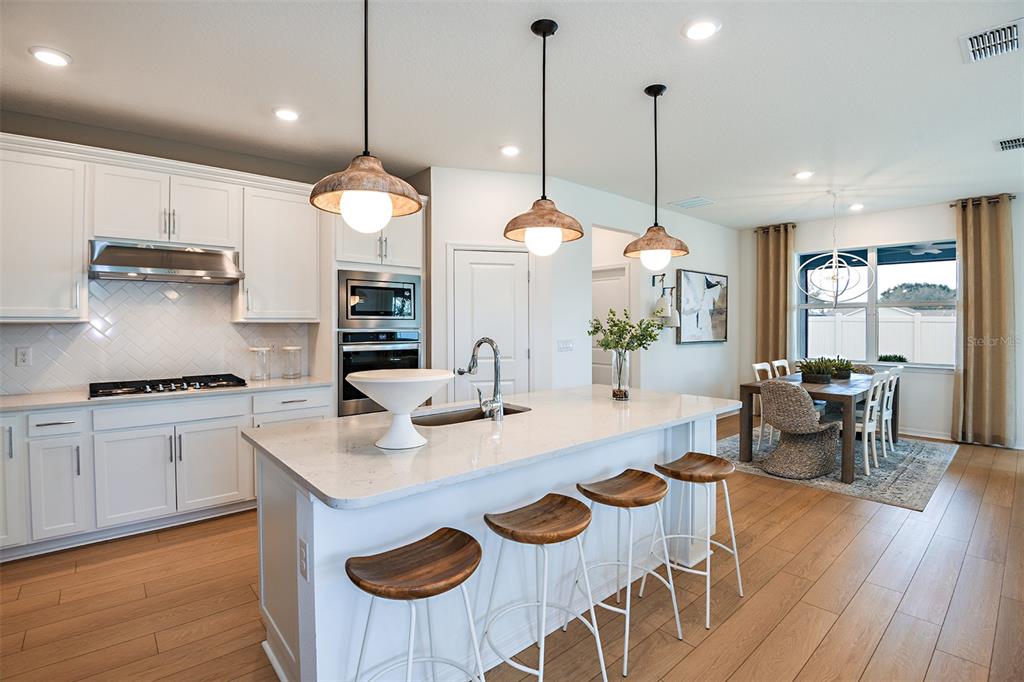 A kitchen features white cabinets, a quartz island with bar stools, and an adjacent dining area — 6574 ASBURY BARNES LANE, WESLEY CHAPEL, FL