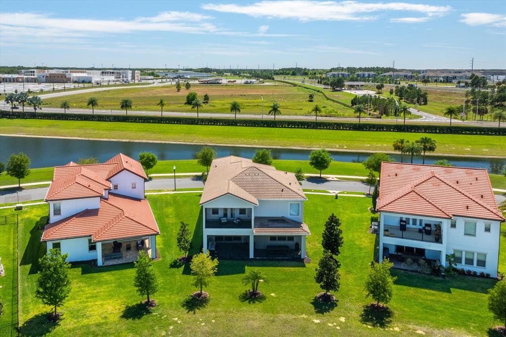 An aerial view shows three houses with red tile roofs overlooking a canal and field — 8222 TOPSAIL PLACE, WINTER GARDEN, FL