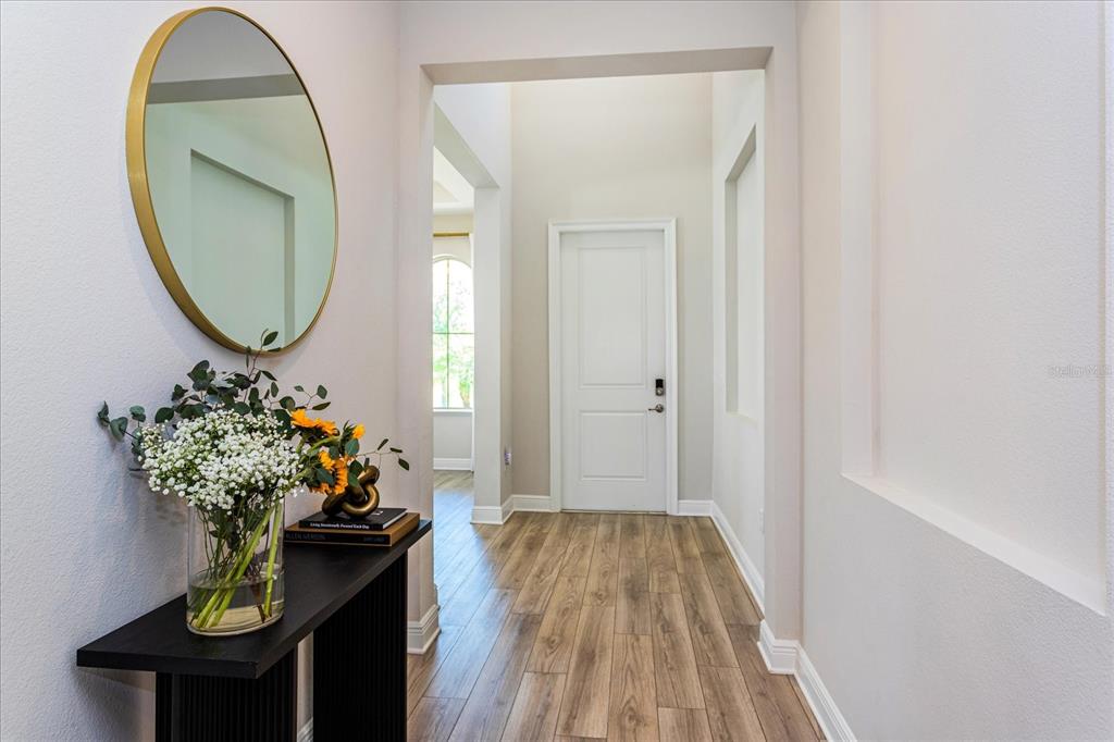 A hallway features light wood flooring, a black console table with flowers, and a round mirror — 8222 TOPSAIL PLACE, WINTER GARDEN, FL