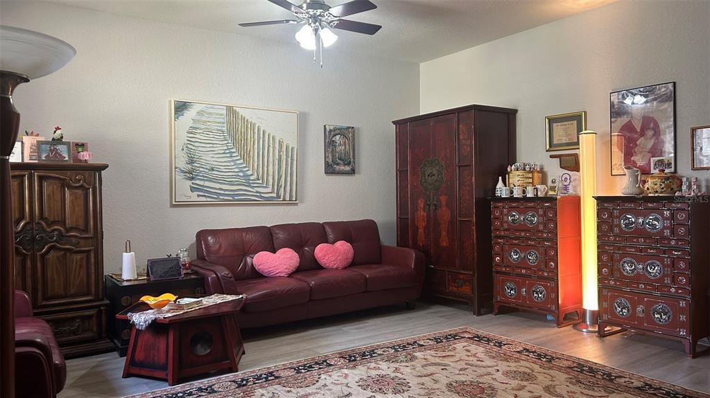 A living room features a red leather sofa, wooden cabinets, a ceiling fan, and area rug — 17334 PROMENADE DRIVE, CLERMONT, FL