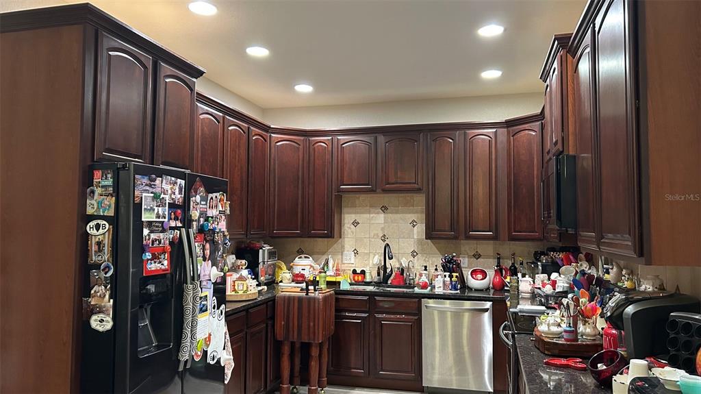 A kitchen features dark wood cabinets, stainless steel appliances, and a tiled backsplash — 17334 PROMENADE DRIVE, CLERMONT, FL