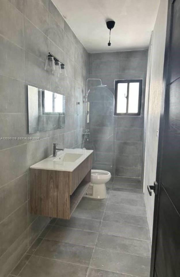 A modern bathroom features gray tiled walls and floors, a floating vanity, and a glass shower — 0 Brisas, FL