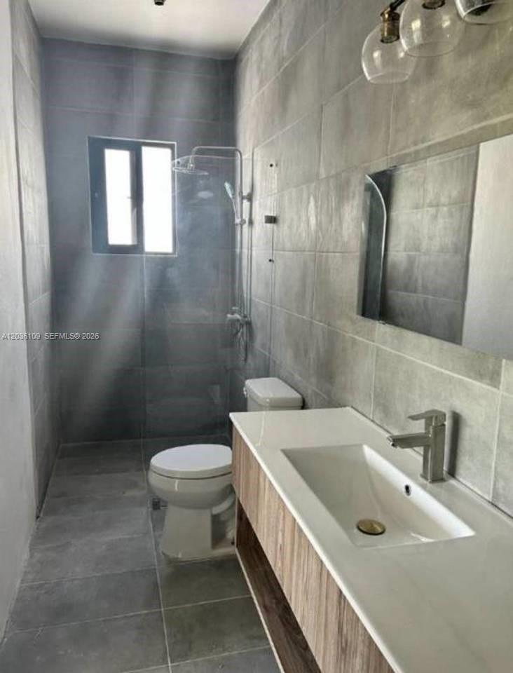 A modern bathroom features gray tiled walls, a glass shower enclosure, and a wood-toned vanity — 0 Brisas, FL