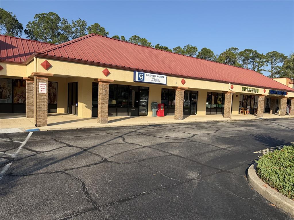A single-story commercial strip mall with a red metal roof and brick-accented pillars — 212 ST JOE PLAZA DRIVE, PALM COAST, FL