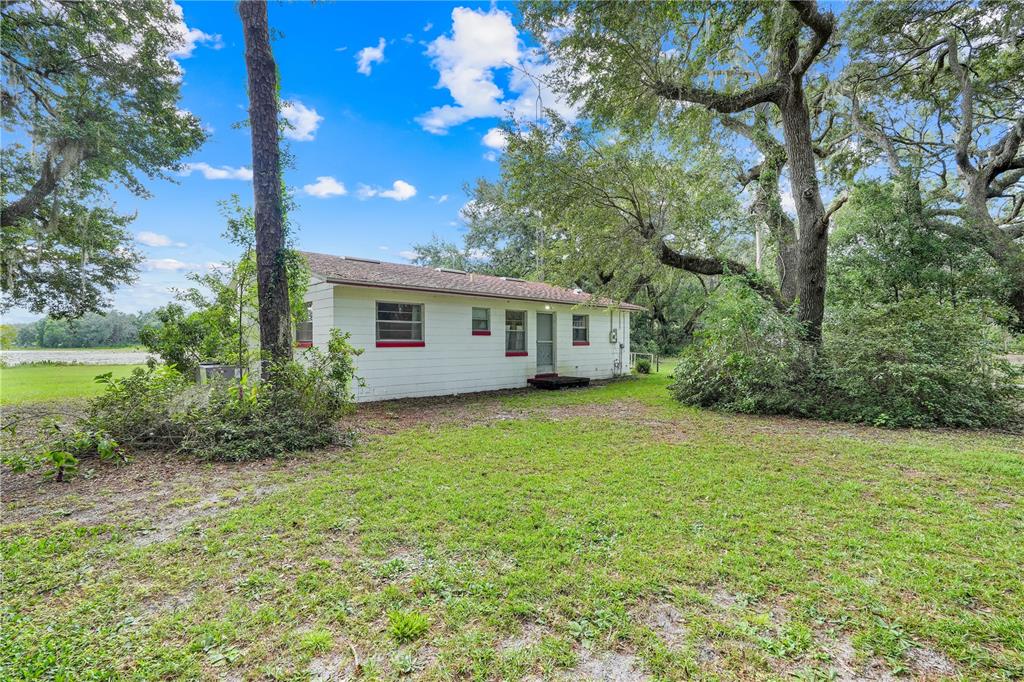 A white, single-story house with red trim sits on a grassy lot under large trees — 1440 SELMAN ROAD, LEESBURG, FL
