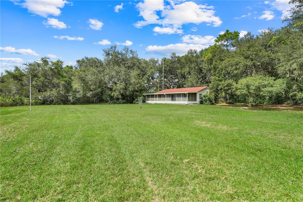 A small house with a screened porch sits on a large, grassy lot near trees — 1440 SELMAN ROAD, LEESBURG, FL