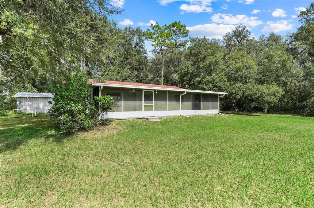 A single-story house with a screened-in porch sits on a large, grassy lot with trees — 1440 SELMAN ROAD, LEESBURG, FL