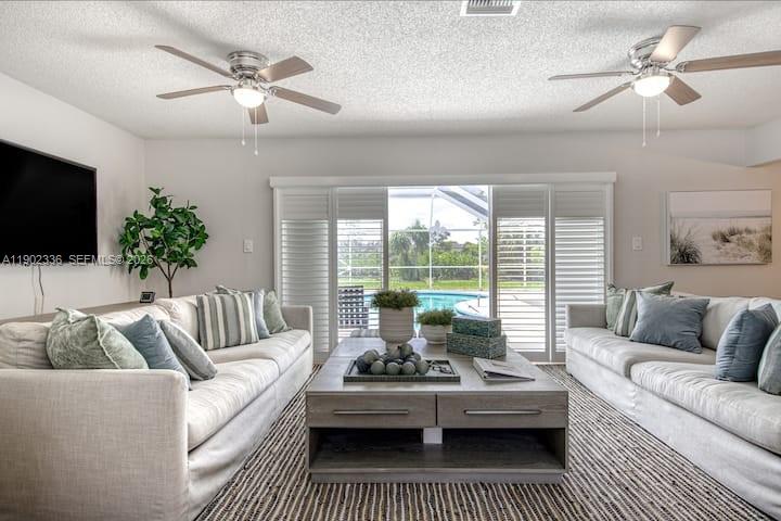 A living room with two sofas, a coffee table, ceiling fans, and sliding glass doors — 1500 NW 45th St, Pompano Beach FL 33064, POMPANO BEACH, FL