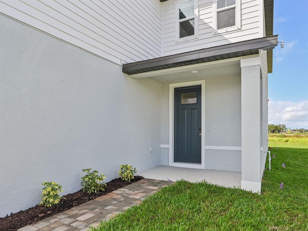 A gray front door sits under a covered porch next to a paved walkway — 11305 BELLEWOOD TERRACE, PARRISH, FL