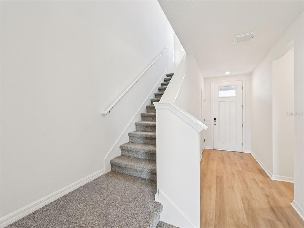 A carpeted staircase leads upward next to a front entryway with light wood-look flooring — 11305 BELLEWOOD TERRACE, PARRISH, FL